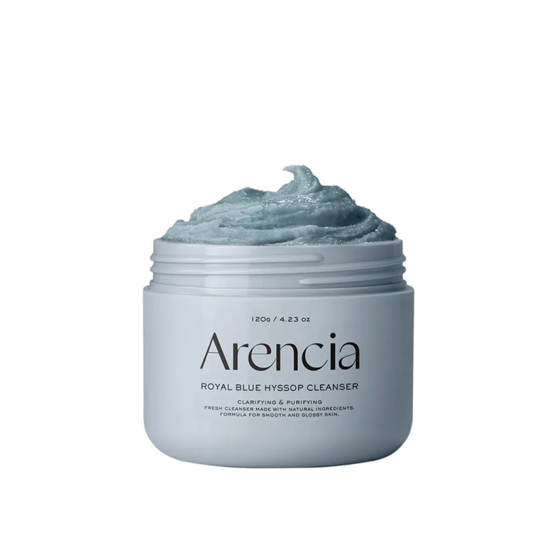 Отворена тегличка со Arencia Royal Blue Hyssop Cleanser – густа кремаста сина формула за прочистување и нега на кожа, поставена на бела позадина. На пакувањето пишува дека е формулирана со природни состојки за сјајна и мазна кожа. An open jar of Arencia Royal Blue Hyssop Cleanser – a thick, creamy blue formula designed for skin cleansing and care, shown on a white background. The packaging highlights natural ingredients for smooth and glossy skin.