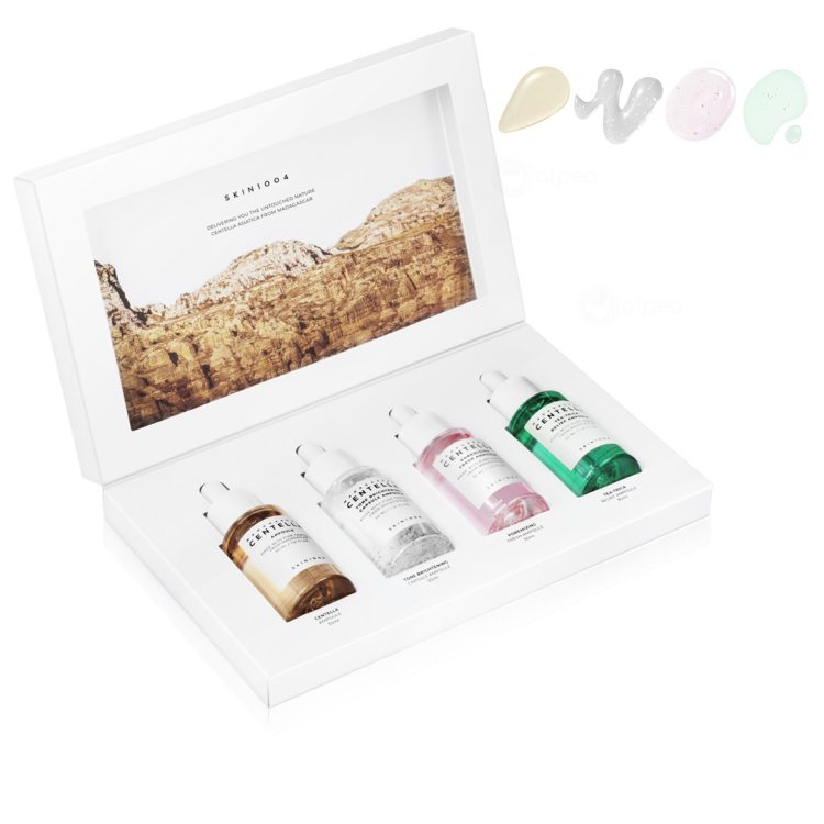 Отворена бела кутија со четири SKIN1004 ампули во различни бои – Centella, Hyalu-Cica, Tone Brightening и Tea-Trica – сместени во елегантен сет со позадина од природни карпи. An open white box containing four SKIN1004 ampoules in various colors – Centella, Hyalu-Cica, Tone Brightening, and Tea-Trica – arranged in an elegant set with a natural rocky landscape in the background.