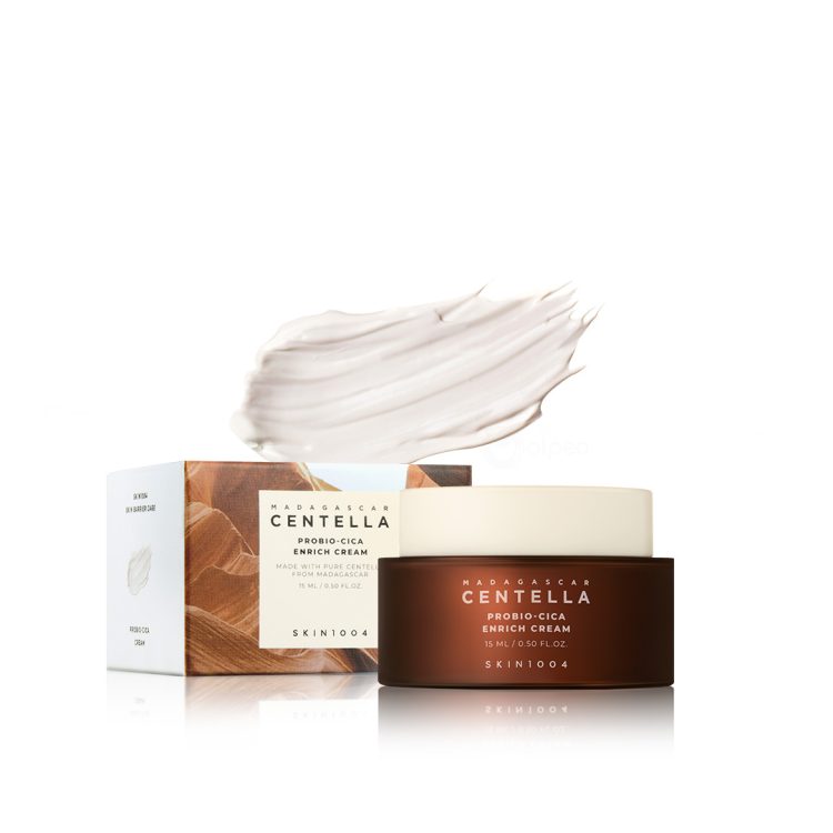 Мини пакување од SKIN1004 Madagascar Centella Probio-Cica Enrich Cream 15ml со тегличка и кутиија прикажани заедно со текстура од кремата во позадина. Mini packaging of SKIN1004 Madagascar Centella Probio-Cica Enrich Cream 15ml with jar and box shown together, along with cream texture in the background.